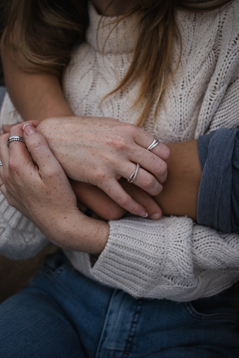 Hands of two people intertwined, wearing rings and sweaters.